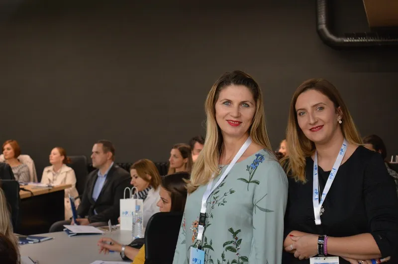 Two attendees wearing lanyards smiling at the camera in the hall