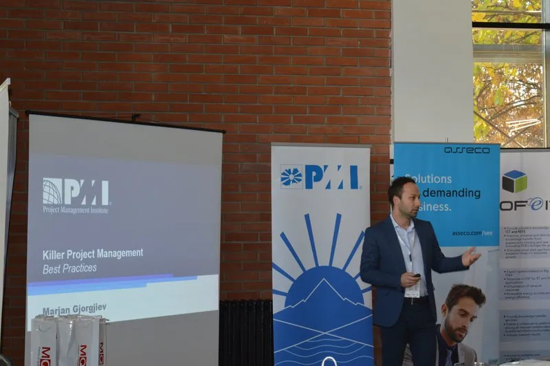 A speaker in front of the slide "Killer Project Management Best Practices", between the screen and the PMI banner