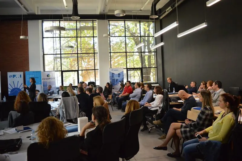 The audience following a presentation, autumn trees behind the tall windows