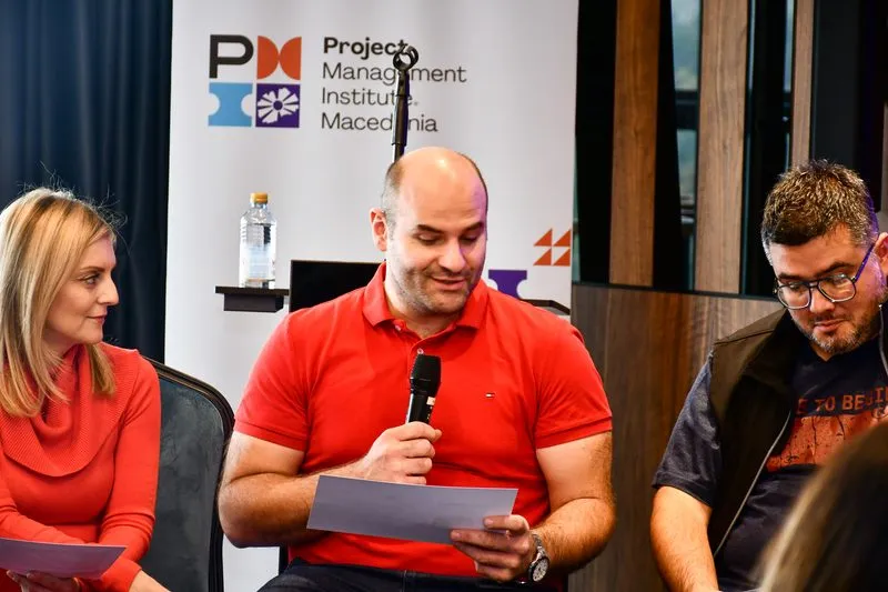 A panel discussion - one participant reading a question from a slip of paper, two others beside him