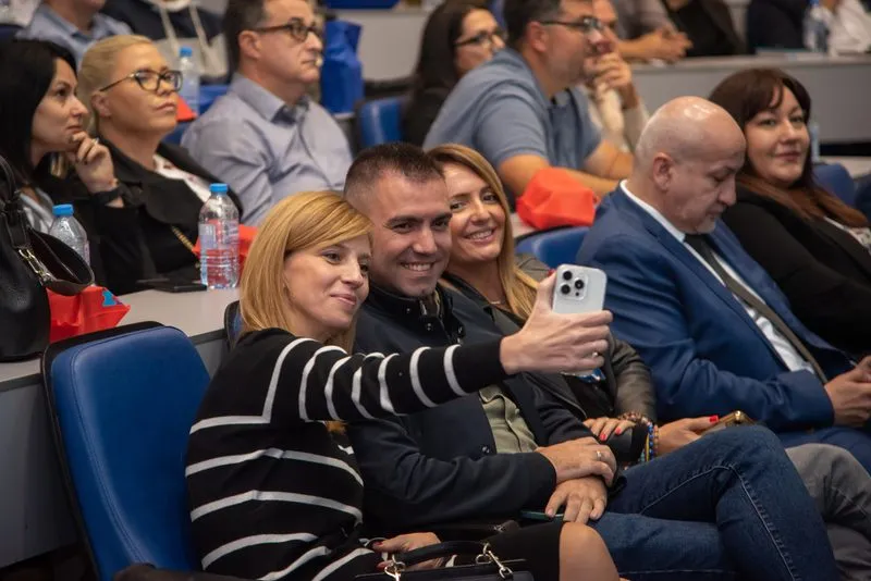 Attendees laughing in the audience, one of them filming the session on a phone